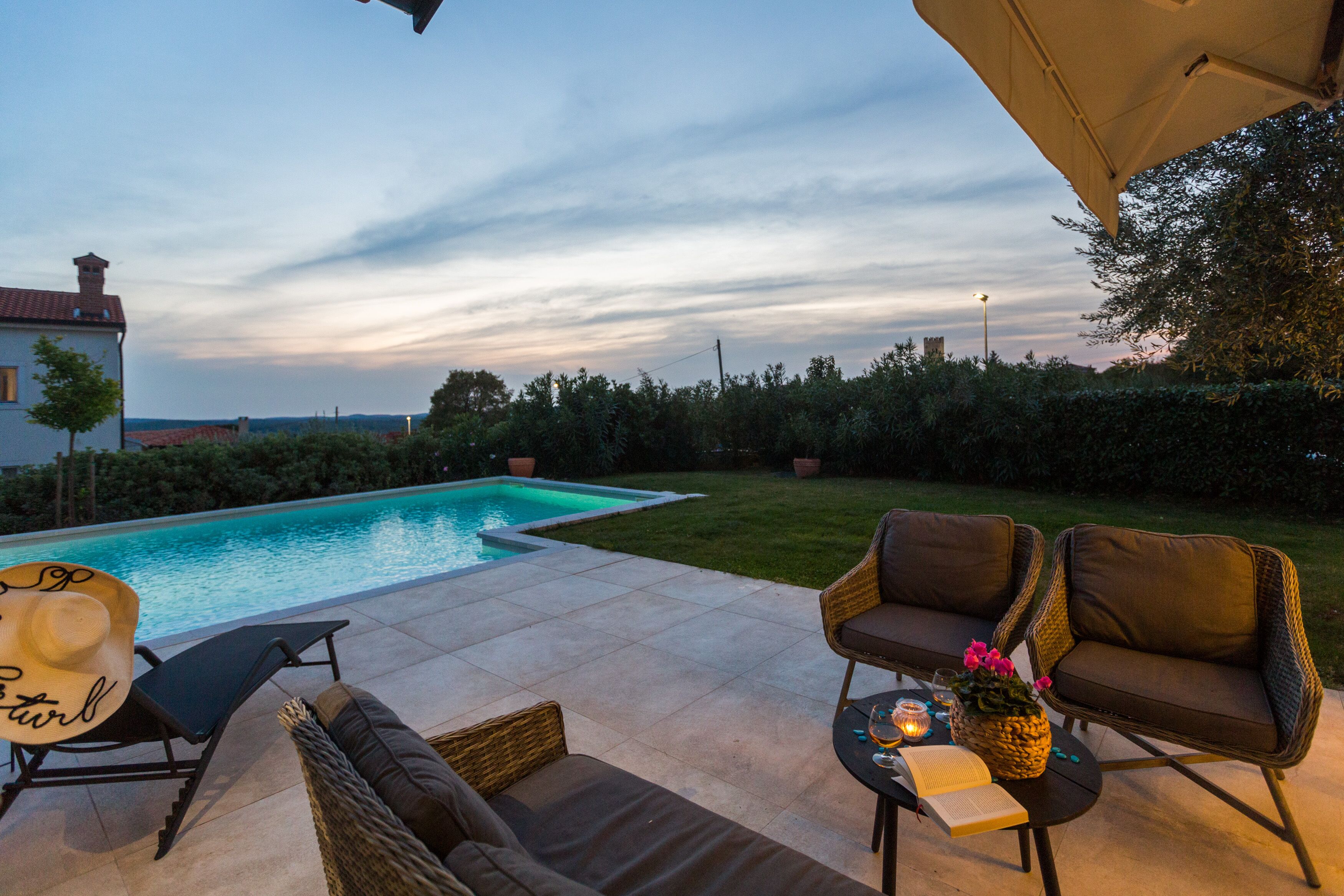 A poolside area with a lounge chair, a wicker sofa, and a table with a book and a candle.