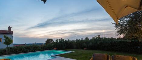 A poolside area with a lounge chair, a wicker sofa, and a table with a book and a candle.