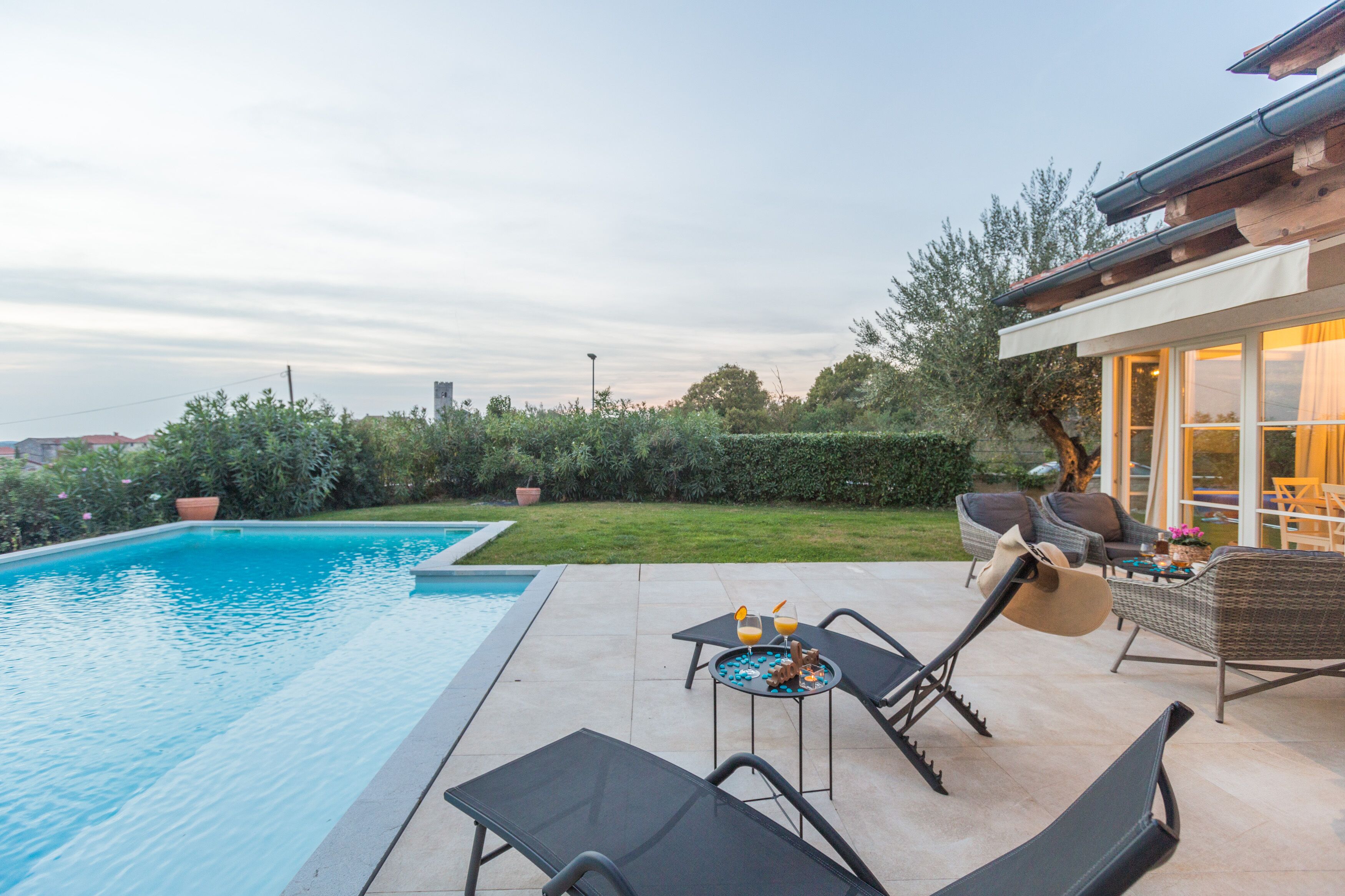 A swimming pool with lounge chairs and a table, surrounded by a well-maintained lawn and a building with large windows.
