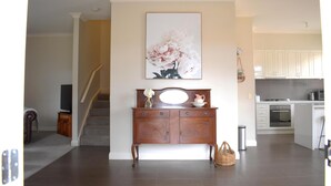 Amplia sala de estar con una consola de madera, un cuadro floral grande y una cocina al fondo.
