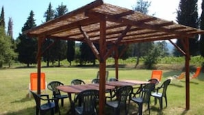 Eine Holz-Pergola mit Tisch und Stühlen in einer grünen Außenanlage.