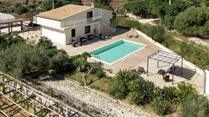 Una casa de dos pisos con piscina, mobiliario exterior y vista al mar.