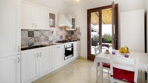 Una cocina con armarios blancos, una estufa y un fregadero. Hay una mesa de comedor con un cojín rojo y un jarrón con flores.