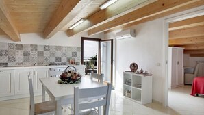 Una cocina moderna con armarios blancos, salpicadero de azulejos y una zona de comedor con mesa y sillas blancas.