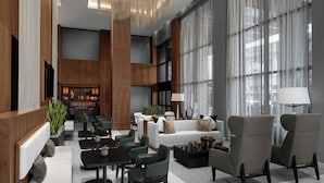 A spacious lobby with a modern design, featuring a seating area with sofas and chairs, a bar area, and large windows providing natural light.