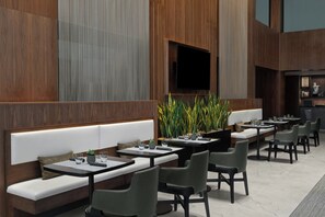 Ein modernes Restaurant mit langen Gemeinschaftstischen, gepolsterten Sitzgelegenheiten und einem großen Fernsehbildschirm.