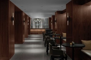 Un interior moderno con paneles de madera, una zona de estar central con mesas y sillas, y una lámpara decorativa.