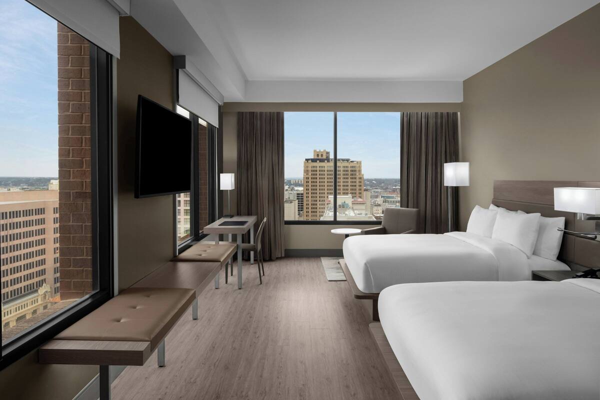 Une chambre d’hôtel avec deux lits, une télévision, un bureau et une vue sur le paysage urbain.
