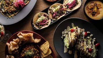 Variedad de platos que incluyen tacos, un tazón de sopa y un plato con un alimento a la parrilla, todo servido en diferentes fuentes.