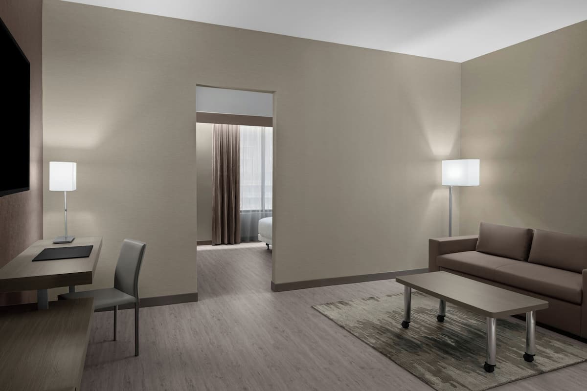 Une chambre d’hôtel moderne au design minimaliste, comprenant un canapé, une petite table, un bureau avec une chaise et un téléviseur.