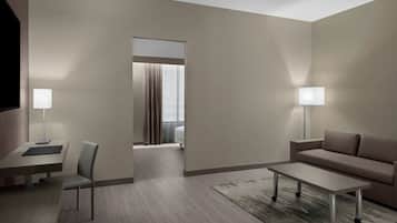 Quarto de hotel moderno com design minimalista, apresentando um sofá, uma pequena mesa, uma escrivaninha com cadeira e uma TV.