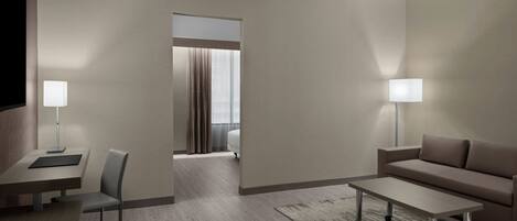 Una habitación de hotel moderna con un diseño minimalista, que incluye un sofá, una mesita, un escritorio con una silla y un televisor.