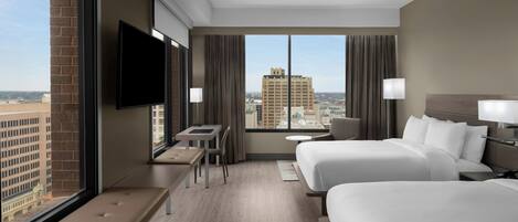 A hotel room with two beds, a TV, a desk, and a view of a cityscape.
