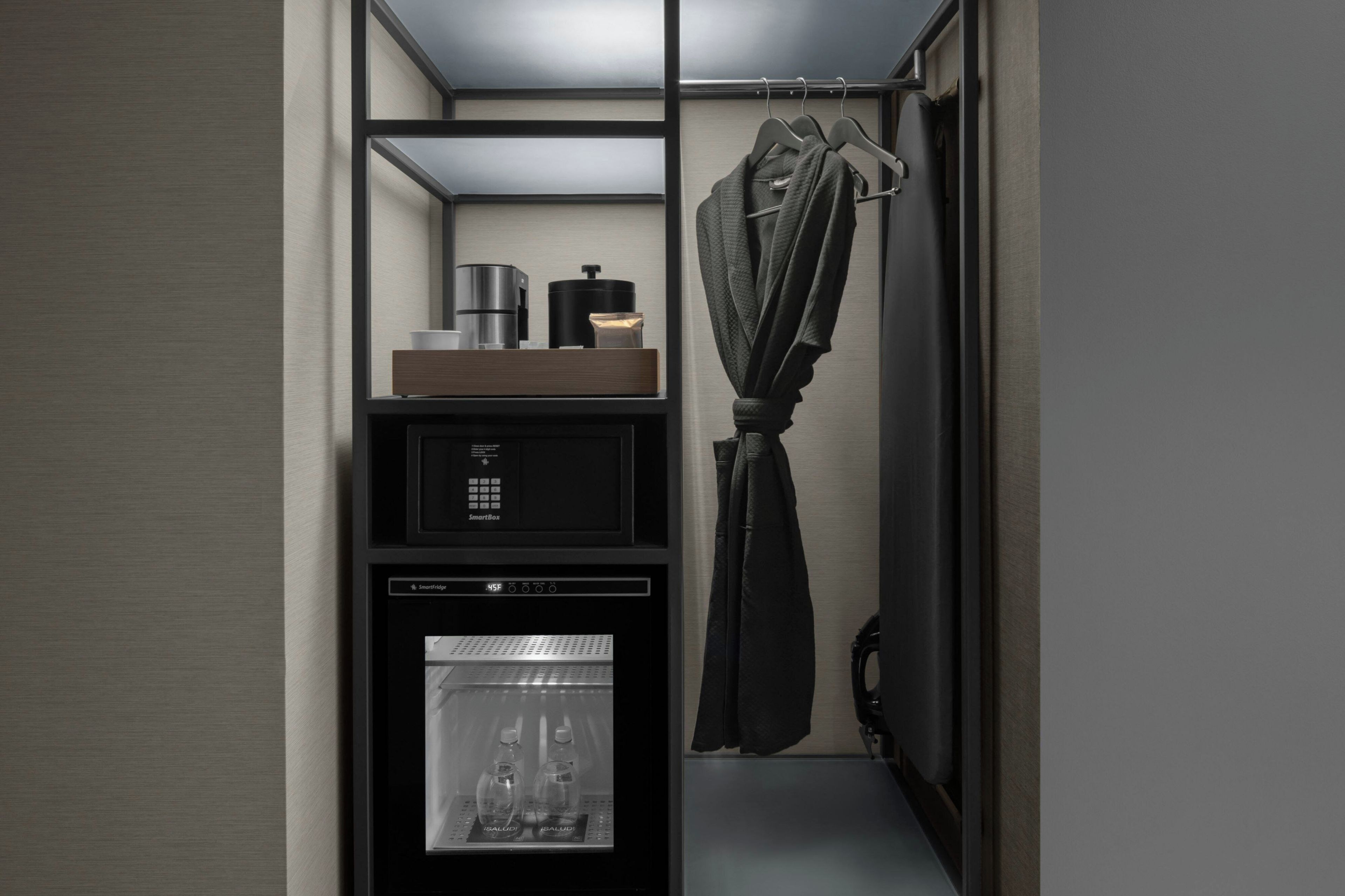 A compact hotel room with a minibar, a refrigerator, and a hanging garment.