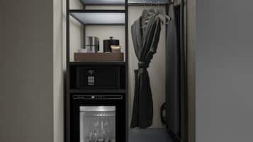 A compact hotel room with a minibar, a refrigerator, and a hanging garment.