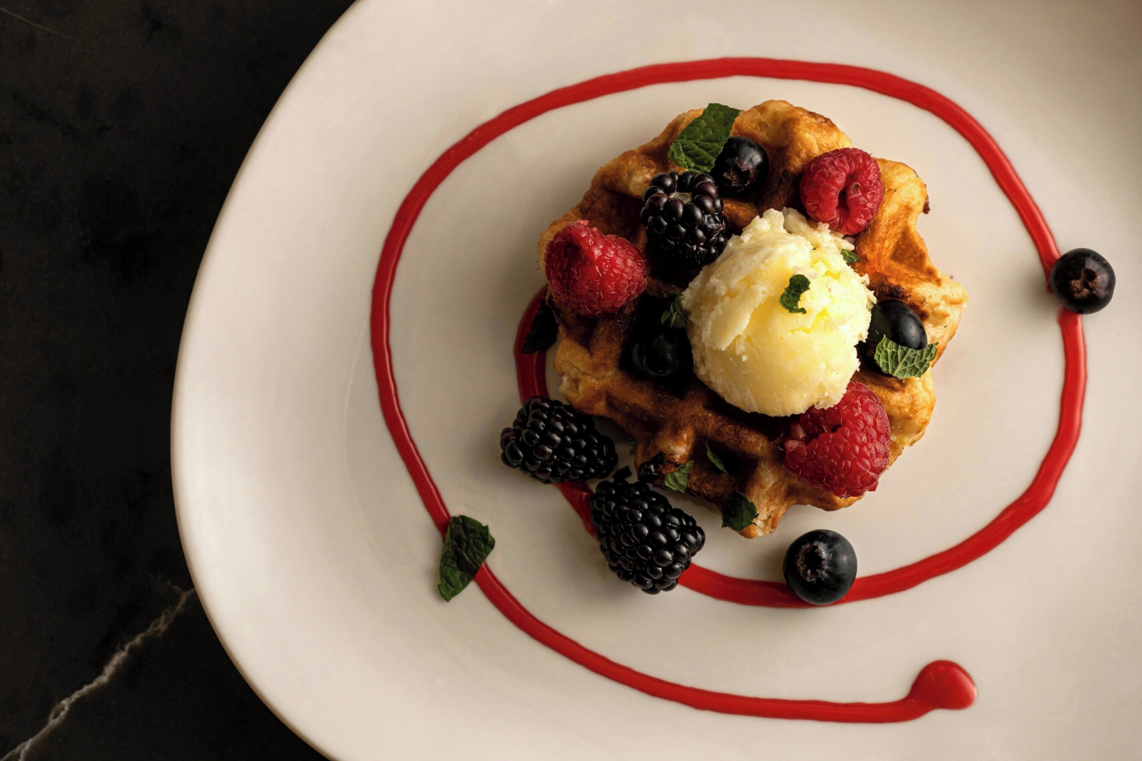 Un plato de postre con gofre, helado y frutos rojos.