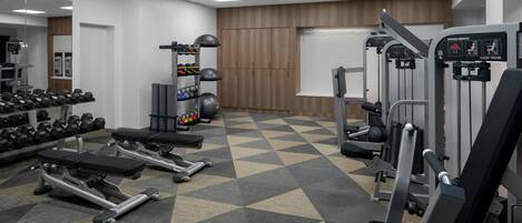 Un gimnasio con máquinas de pesas, mancuernas y un espejo grande.