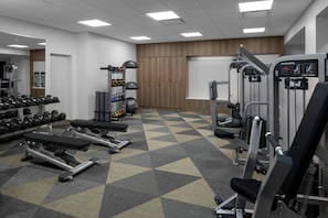 Ein Fitnessstudio mit Kraftgeräten, Kurzhanteln und einer Spiegelwand.