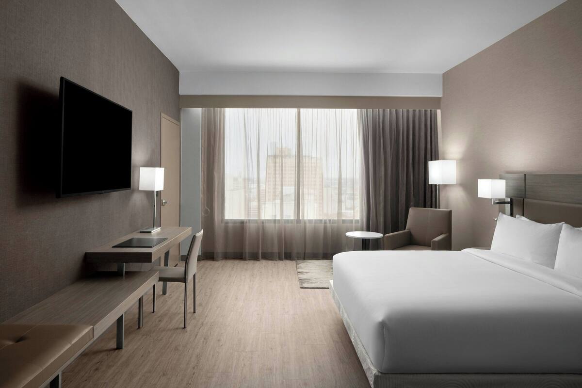Une chambre d’hôtel équipée d’un lit, d’un bureau, d’une chaise, d’une télévision et d’une fenêtre avec des rideaux.