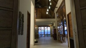 Un vaste hall d’entrée avec un plafond haut, des poutres en bois et des luminaires suspendus.