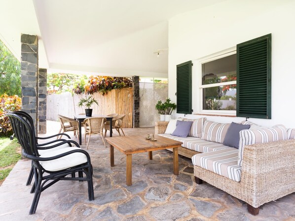 A covered patio area with stone flooring, wicker furniture, and a wooden table. - CORONEL - CASERÍO DE GUAZA (Palm-Mar)