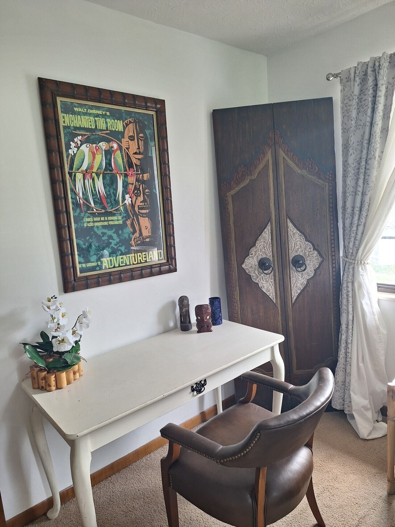 A room with a white desk, a brown leather chair, a poster on the wall, and a decorative cabinet.