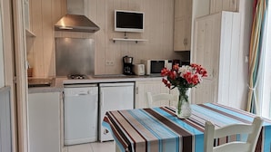 A compact kitchen with a microwave, toaster, and coffee maker. There is a dining table with a striped tablecloth and a vase of flowers.