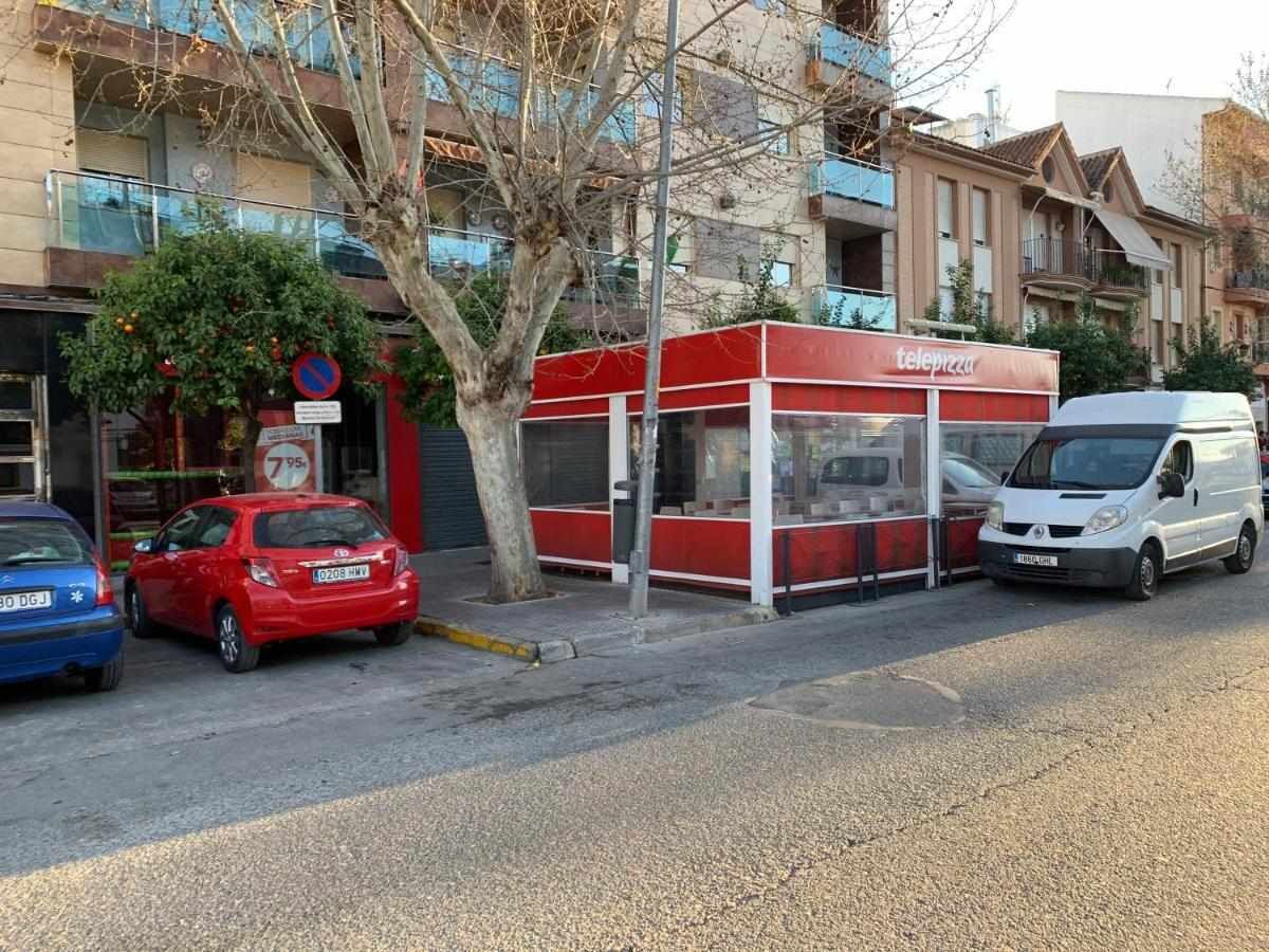 A red and white telephone booth on a street with parked cars and buildings in the background.