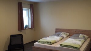 A bedroom with a bed, a chair, a window with curtains, and a ceiling light. - Schoppenstube May (Weigenheim)