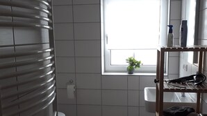 A bathroom with a toilet, a sink, a window, and a shelf with toiletries. - Schoppenstube May (Weigenheim)