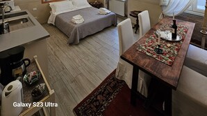 A hotel room with a bed, a desk, a chair, a table with a candle and wine glass, and a painting on the wall. - San Lorenzo Apartment (Firenze)