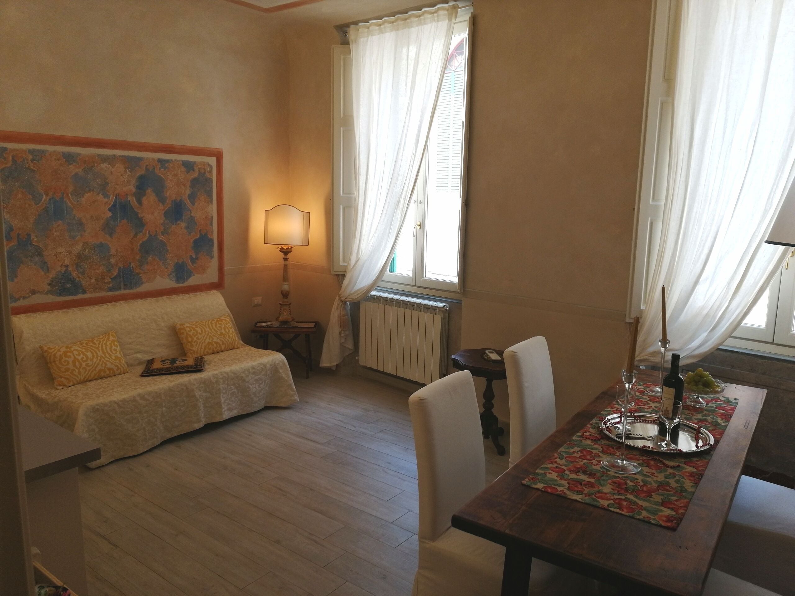 Une pièce chaleureuse avec un canapé, une table à manger agrémentée d’un chemin de table à motifs floraux et une lampe.