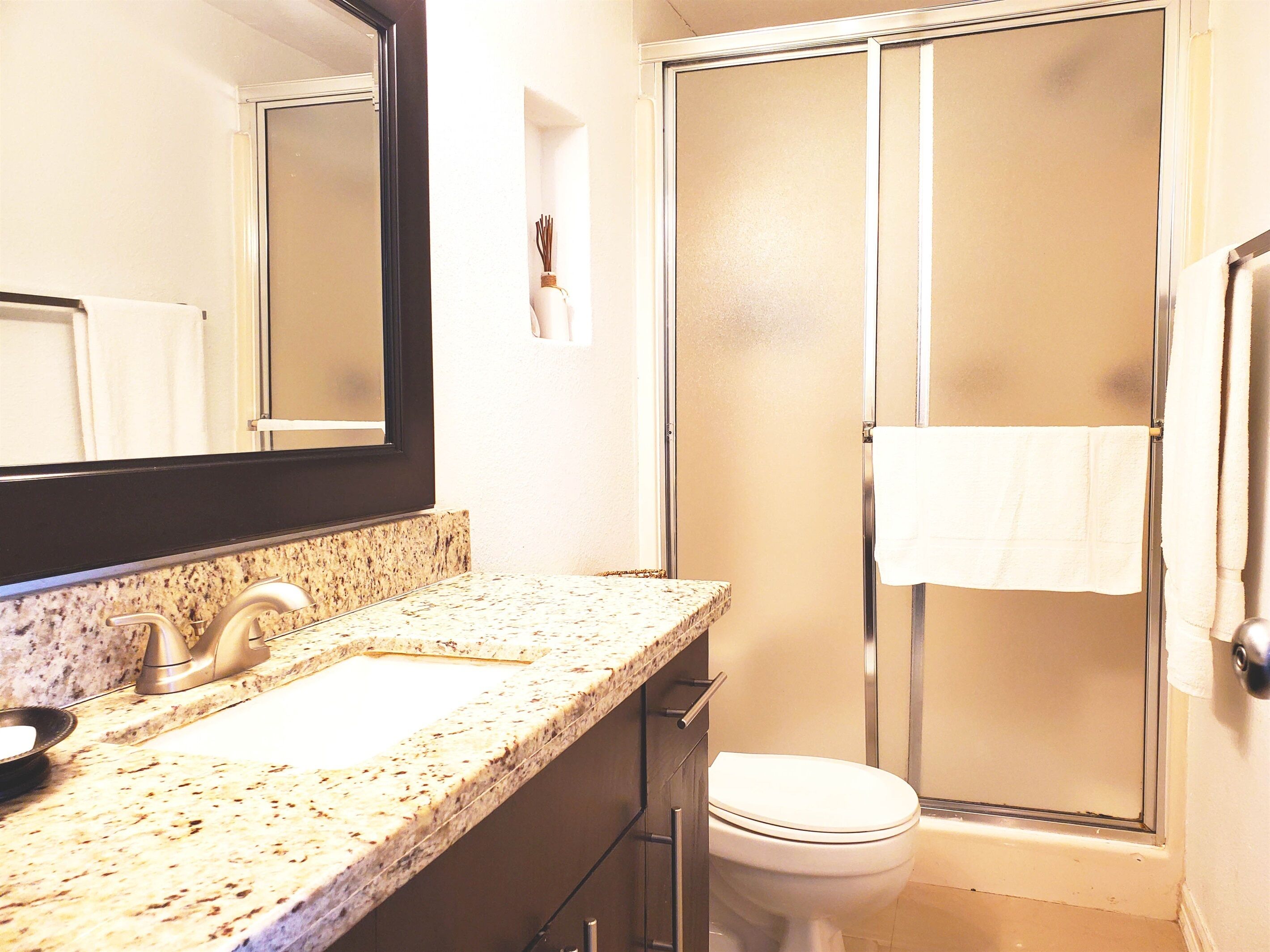 A bathroom with a granite countertop, a sink, a mirror, a toilet, and a glass shower enclosure.