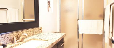 A bathroom with a granite countertop, a sink, a mirror, a toilet, and a glass shower enclosure.