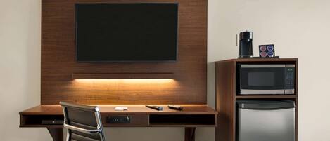 Habitación de hotel con escritorio de madera, televisión de pantalla plana, microondas y refrigerador.