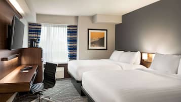 A hotel room with a desk, two beds, a TV, and a window with curtains.
