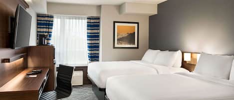 A hotel room with a desk, two beds, a TV, and a window with curtains.