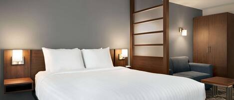 A hotel room with a large bed, a nightstand, a desk, a chair, and a wardrobe.