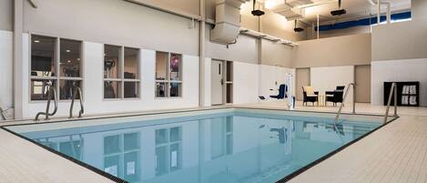 A large indoor swimming pool with clear water, surrounded by tiled walls and windows.