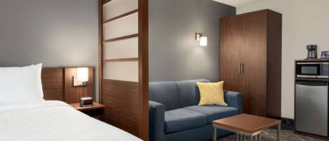 A hotel room with a bed, a sofa, a small table, a microwave, and a cabinet.