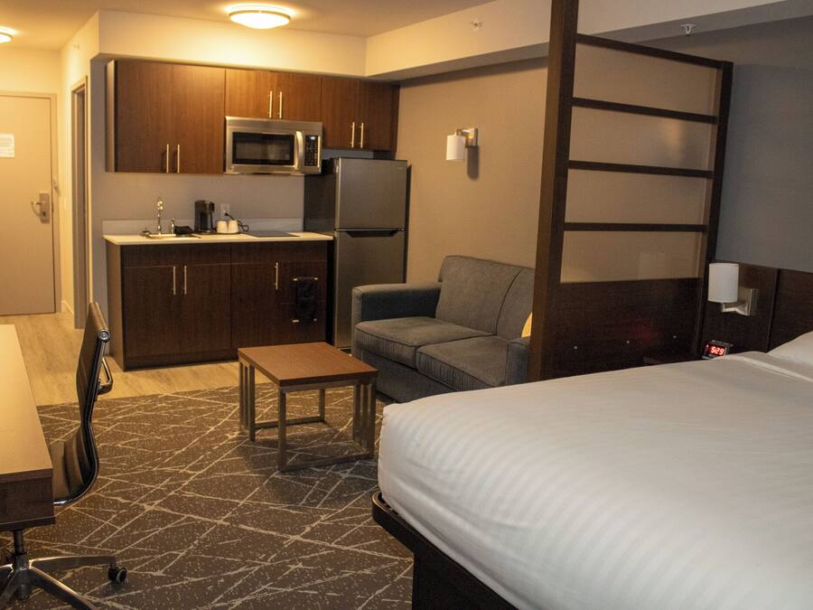 Habitación de hotel compacta con kitchenette, una cama individual, una mesita y una silla.