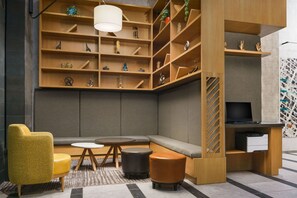 Un área de descanso moderna con un sofá, un sillón amarillo, una mesa redonda y un televisor sobre un soporte de madera.