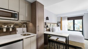 Una habitación de hotel moderna con kitchenette, una cama con vista a la ciudad y una pequeña zona de bar.