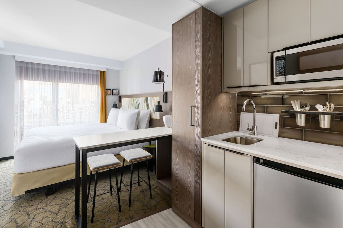A hotel room with a bed, a small kitchenette, and a view of bicycles outside.