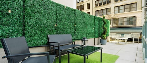 An outdoor seating area with a green wall, a table, and chairs.