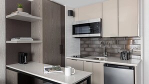 Una cocina moderna con microondas integrado, electrodomésticos de acero inoxidable y un pequeño comedor con una mesa blanca y dos sillas.