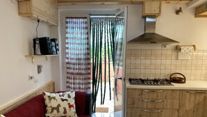 A compact kitchen with a gas stove, wooden cabinets, and a red sofa with patterned cushions. - Apartment - Sleeps 3 & Swimming Pool (Realmonte)