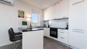A modern kitchen with white cabinets, a black countertop, and stainless steel appliances. There is a window providing natural light and a view of the outdoors. - Apartment Birgir in Sukošan (Sukosan)