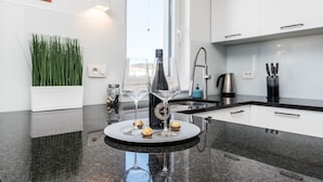 A modern kitchen with a granite countertop, a bottle of champagne, two wine glasses, and a decorative plate with chocolates. - Apartment Birgir in Sukošan (Sukosan)