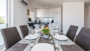 A dining area with a table set for four, a potted plant, and a kitchen in the background. - Apartment Birgir in Sukošan (Sukosan)